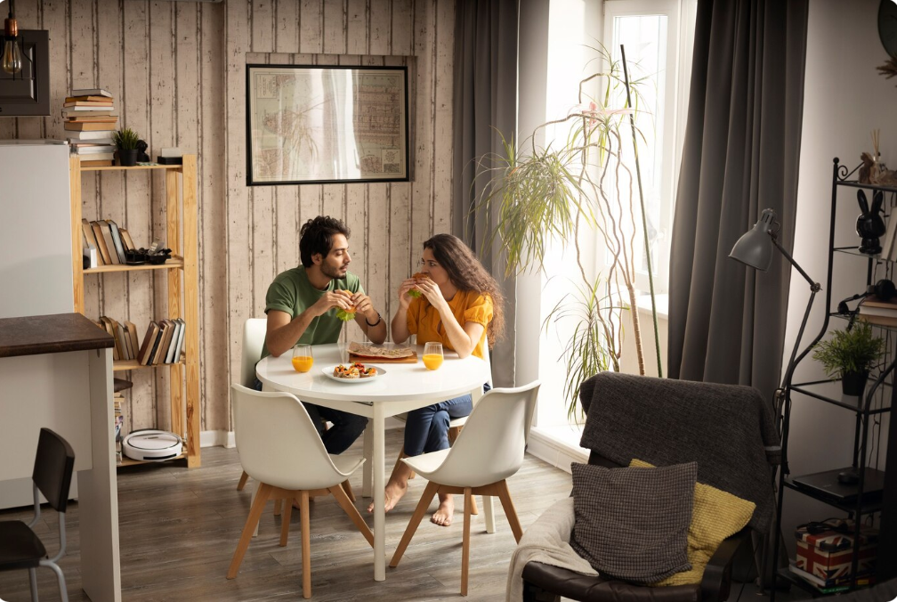 Couple déjeunant dans un salon lumineux avec des murs clairs et une grande fenêtre, illustrant un petit espace optimisé.